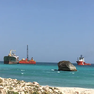 Two barges head to a dry dock on either side. There is a large rock in the foreground.